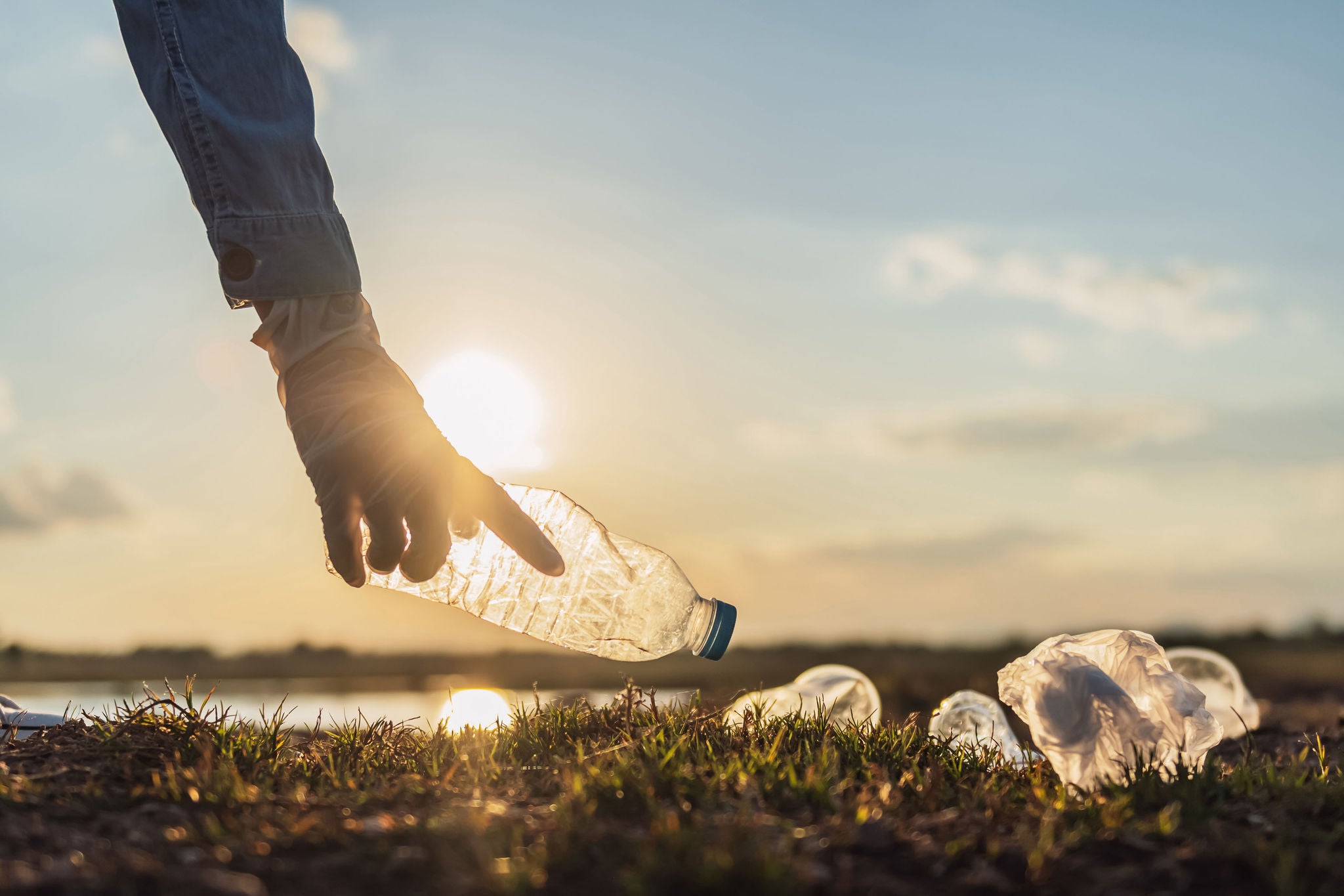 Hand reaching for plastic bottle in front of sunset